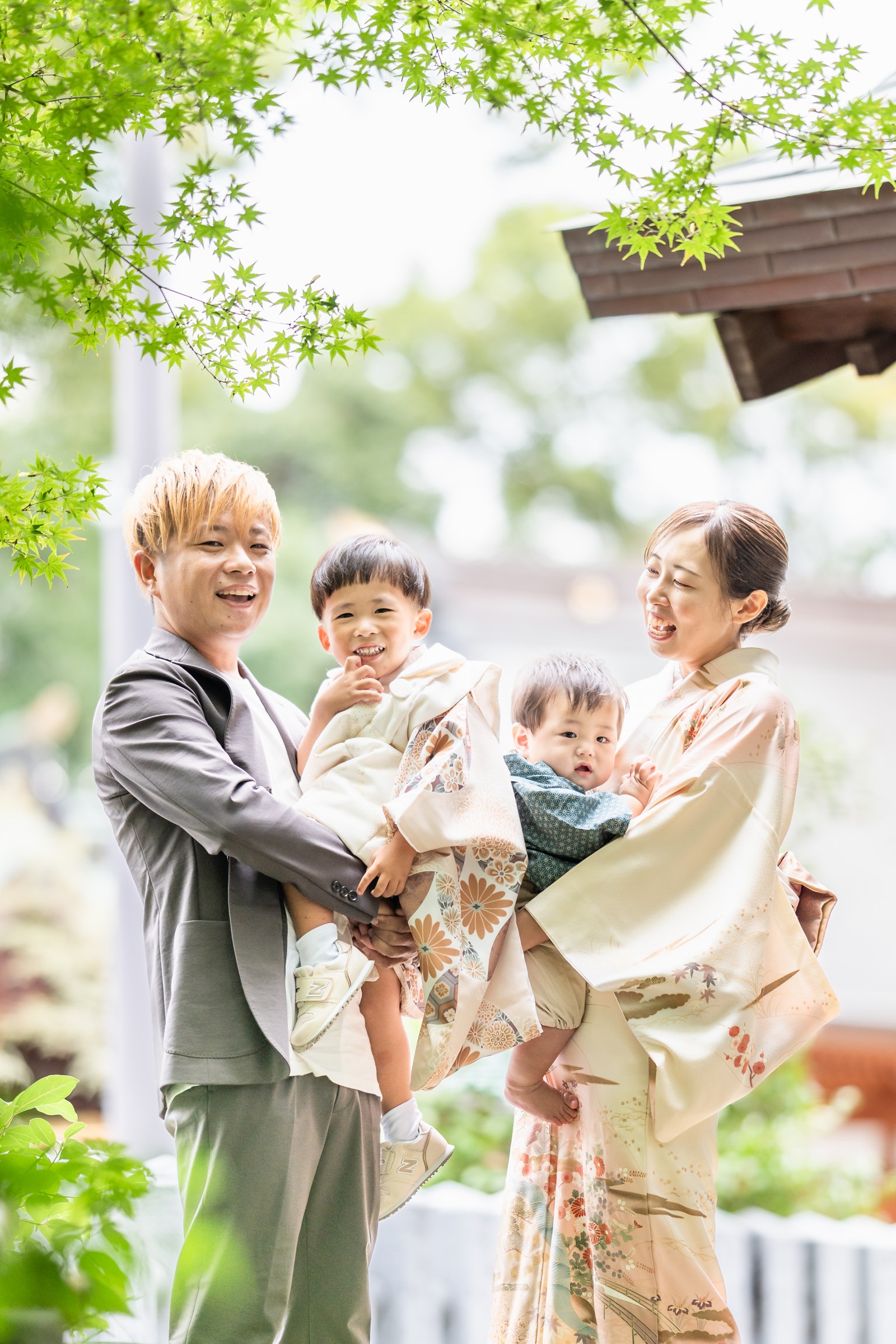 緑のもみじに囲まれて、七五三の晴れ着姿のお子さまと家族4人で写る記念写真